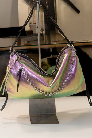 Iridescent INA KENT handbag with studded accents and a black strap displayed on a metal stand in a well-lit indoor setting.