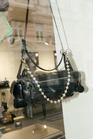 An INA KENT black leather handbag with a zipper, beaded chain strap, and attached keychains is stylishly displayed in a store window.