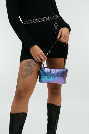 Person in schwarzem Kleid und Stiefeln, mit schillernder Handtasche von INA KENT, Kettengürtel und Schlangentattoo auf dem Oberschenkel.