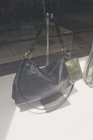An INA KENT black leather handbag with a large strap and a small metallic pouch attached is displayed on a stand in a store window.