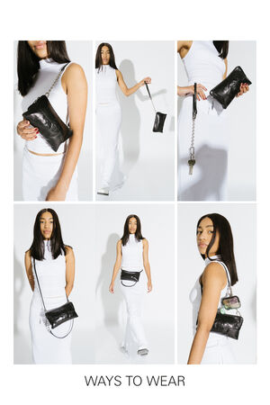 Eine Frau in einem weißen Kleid demonstriert sechs Tragevarianten der schwarzen INA KENT-Tasche mit silberner Kette, die als Clutch, Crossbody, Schultertasche und Gürteltasche getragen werden kann. Der Text lautet "Ways To Wear".