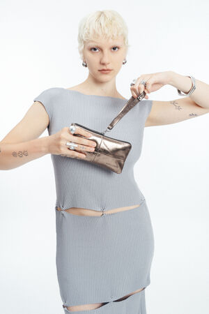 Eine Person mit kurzen blonden Haaren trägt ein hellgraues geripptes Kleid mit Ausschnitten und hält eine INA KENT Metallic-Clutch-Tasche in der Hand, die sie vor einem schlichten weißen Hintergrund öffnet.