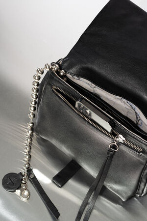 INA KENT Tasche aus schwarzem Leder mit metallischer Kugelkette, Reißverschluss und einer offenen Tasche, in der ein silbernes Smartphone steckt.