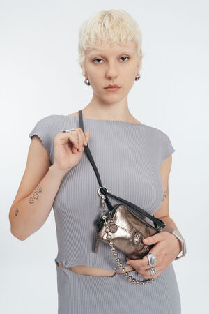 Eine Person mit kurzen blonden Haaren trägt ein graues, geripptes Kleid und hält eine INA KENT Metallic-Tasche über der Schulter. Sie hat sichtbare Tattoos und Silberschmuck.