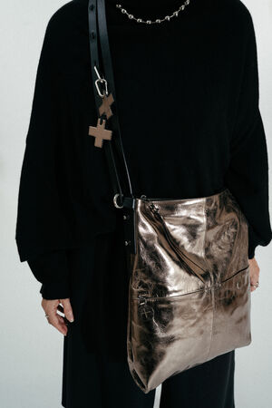 Person trägt ein schwarzes Outfit mit einer INA KENT Metallic-Bronze Crossbody Bag mit kreuzförmigen Schlüsselanhängern am Riemen.