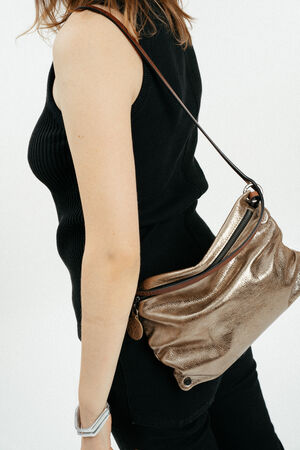 A person wearing a sleeveless black top and black pants carries an INA KENT metallic gold shoulder bag.