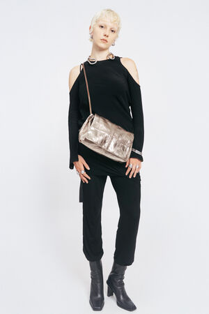 Person with short blond hair stands against a white background, wearing a black cold-shoulder outfit, black boots, and an INA KENT metallic crossbody bag.