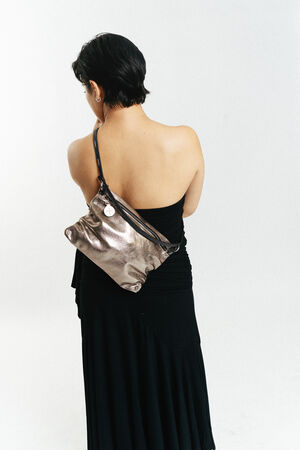 A person with short dark hair wearing a black one-shoulder dress stands with their back to the camera, carrying an INA KENT metallic shoulder bag.