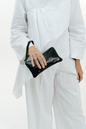Person in a white outfit holding an INA KENT black leather wristlet bag against a plain white background.