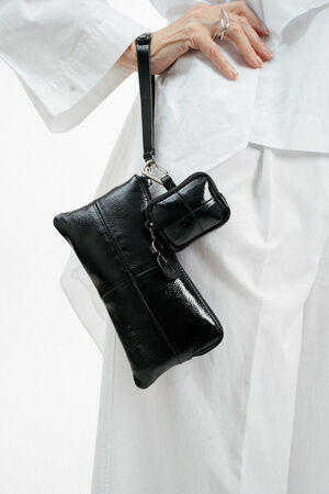 Eine weiß gekleidete Person hält ein schwarzes, glänzendes Lederarmband von INA KENT und eine kleine, passende Tasche, die mit einem Riemen befestigt ist.