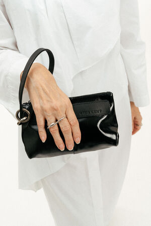 Person in weißer Kleidung, die eine kleine schwarze INA KENT-Ledertasche in der linken Hand hält und einen silbernen Ring trägt.