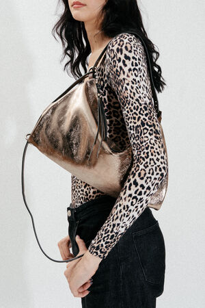 Weiblich gelesenes Model mit dunklen Haaren trägt goldene Ledertasche auf der Schulter