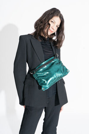 Person wearing a black suit and black top stands against a white background, featuring a shiny green INA KENT crossbody bag worn across the chest.