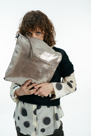 Weiblich gelesenes Modell mit großer goldenen Tasche vor dem Gesicht