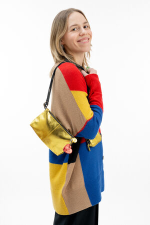 Woman in a colorful sweater with red, yellow, blue, and brown blocks, smiling and holding a metallic gold INA KENT shoulder bag against a plain white background.