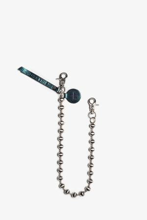 Eine Metallperlenkette mit Karabinerverschlüssen an beiden Enden, die an einem Lederanhänger und einem runden Lederstück mit einem Pluszeichen befestigt ist, zeigt die charakteristischen INA KENT-Details.