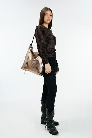 weiblich gelesenes Model mit goldener, großen Ledertasche auf der Schulter