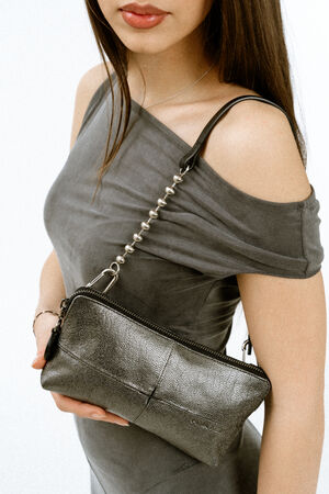 Weiblich gelesenes Modell in grauem Kleid mit einer kleinen Schultertasche aus Leder und schwarzem Riemen mit metallischen Kugelelementen