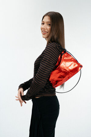 Weiblich gelesenes Model mit roter, glänzenden Ledertasche auf der Schulter