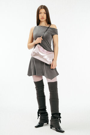 Weiblich gelesenes Model in grauem Kleid mit rosa, metallischen Tasche aus Leder auf der Schulter