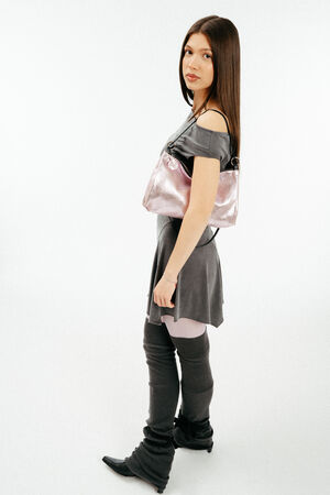 Weiblich gelesenes Model in grauem Kleid mit rosa, metallischen Tasche aus Leder auf der Schulter