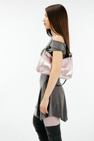 Weiblich gelesenes Model in grauem Kleid mit rosa, metallischen Tasche aus Leder auf der Schulter