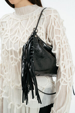 Weiblich gelesenes Model in losem, weißen Strick, mit schwarzer Ledertasche mit Fransen auf der Schulter