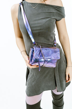 A woman wearing a one-shoulder grey dress holds an INA KENT shiny purple crossbody bag. She also wears light purple tights and a necklace.