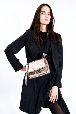 Woman in a black outfit stands against a white background, wearing an INA KENT metallic crossbody bag with a wide strap.
