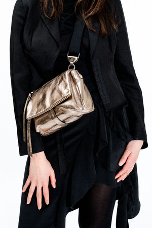 A person wearing a black outfit holds an INA KENT metallic gold crossbody bag, with the bag resting at their hip against a plain white background.