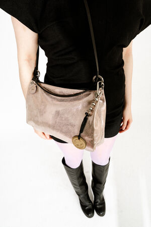 Person wearing a black dress, white tights, and black boots, holding an INA KENT metallic shoulder bag with a round gold keychain, photographed from above.