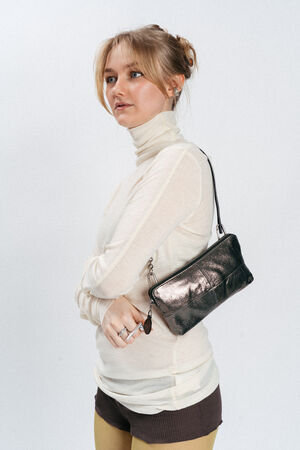 A woman wearing a sheer white turtleneck, yellow tights, and brown shorts stands with arms crossed, holding an INA KENT small black handbag over her shoulder against a plain background.