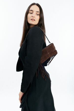 Woman with long brown hair wearing a black outfit and carrying an INA KENT dark brown fringed shoulder bag, looking over her shoulder against a white background.