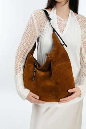 A woman wearing a white lace-sleeve top and skirt holds a large brown INA KENT suede shoulder bag with a black strap.