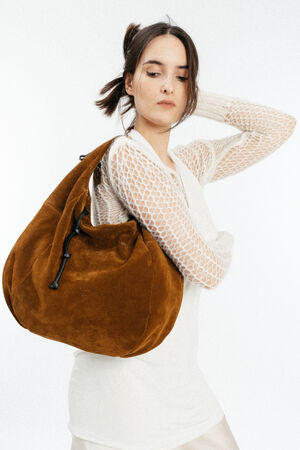 Woman in a white mesh long-sleeve top poses with a large brown INA KENT suede shoulder bag against a plain white background.