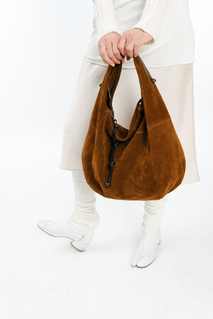A person wearing a white outfit holds a large brown suede INA KENT handbag with black handles.