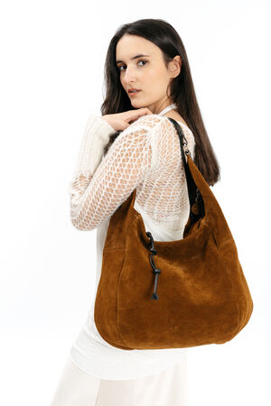 Woman with long dark hair wearing a white knit sweater and holding a large brown suede INA KENT shoulder bag, looking over her shoulder against a white background.