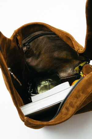 Open brown suede INA KENT bag with a zippered inner pocket, containing a green wallet, a notebook, and other small items.