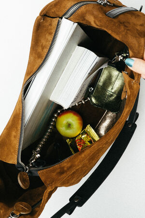 An open brown suede INA KENT bag containing a book, a wallet, a set of keys, an apple, and a wrapped candy.