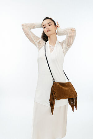 Woman in a white dress poses with her hands behind her head, wearing an INA KENT brown suede fringe crossbody bag against a plain white background.