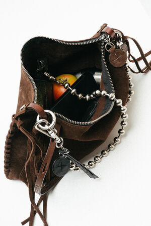 Open brown suede INA KENT bag with a zipper, containing a smartphone, a red and yellow fruit (possibly an apple), and a beaded chain accessory visible inside.