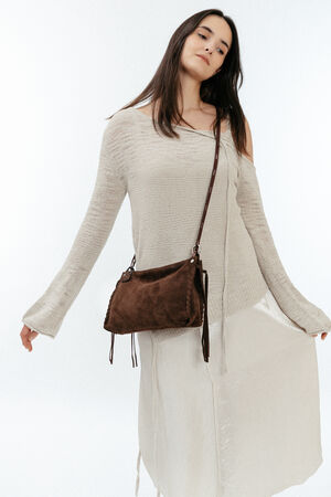 A woman in a light beige knit dress poses with an INA KENT brown suede crossbody bag against a plain white background.