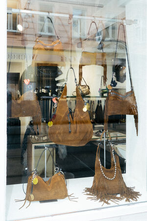 Ein Schaufenster mit mehreren INA KENT-Handtaschen aus braunem Leder mit Fransen und dekorativen Anhängern, die in Regalen angeordnet sind und an Haken hängen.