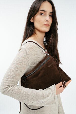 Woman with long dark hair wearing a light beige textured top holds an INA KENT dark brown suede handbag with zipper and tassel detail under her arm.