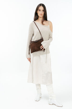Woman wearing a cream-colored, off-shoulder sweater and skirt, white boots, and leg warmers, carrying an INA KENT brown crossbody bag, standing against a white background.