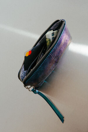 A small zippered pouch by INA KENT with a teal strap holds a black credit card and paper currency, shown lying on a flat surface.
