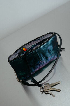 A metallic teal INA KENT zippered purse with a black strap sits on a gray surface, partially unzipped, with a set of five keys attached to the strap.
