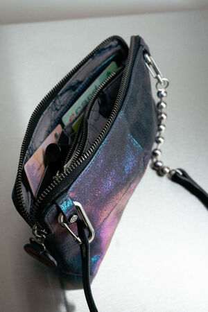 A small iridescent INA KENT purse with a zipper is open, revealing a few cards and a tube of lip balm inside.