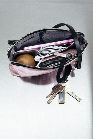 A small open INA KENT purse with a set of keys, a brown round object, a phone, and white earphones partially visible inside.