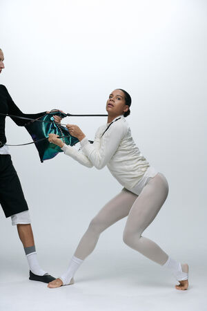 Zwei Tänzerinnen in weißer und schwarzer Tanzkleidung ziehen an den gegenüberliegenden Enden einer bunten INA KENT-Tasche vor einem schlichten hellen Hintergrund.